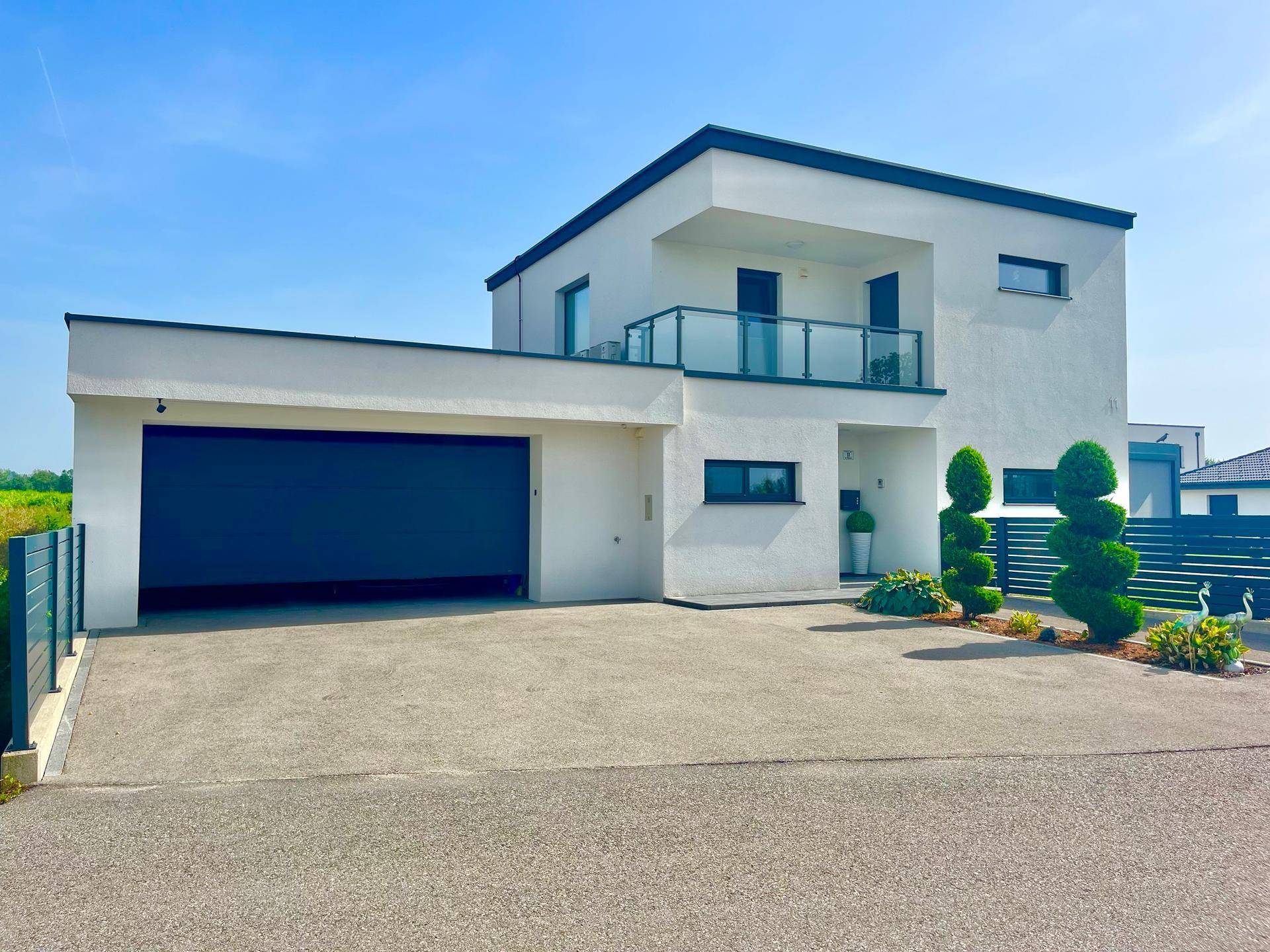 Moderne Villa mit Doppelgarage und gepflegter Auffahrt unter blauem Himmel.