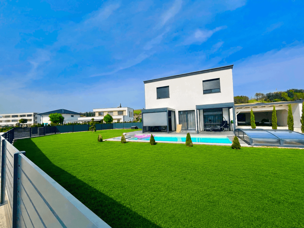Großer, gepflegter Garten mit Pool und moderner Architektur im Hintergrund.