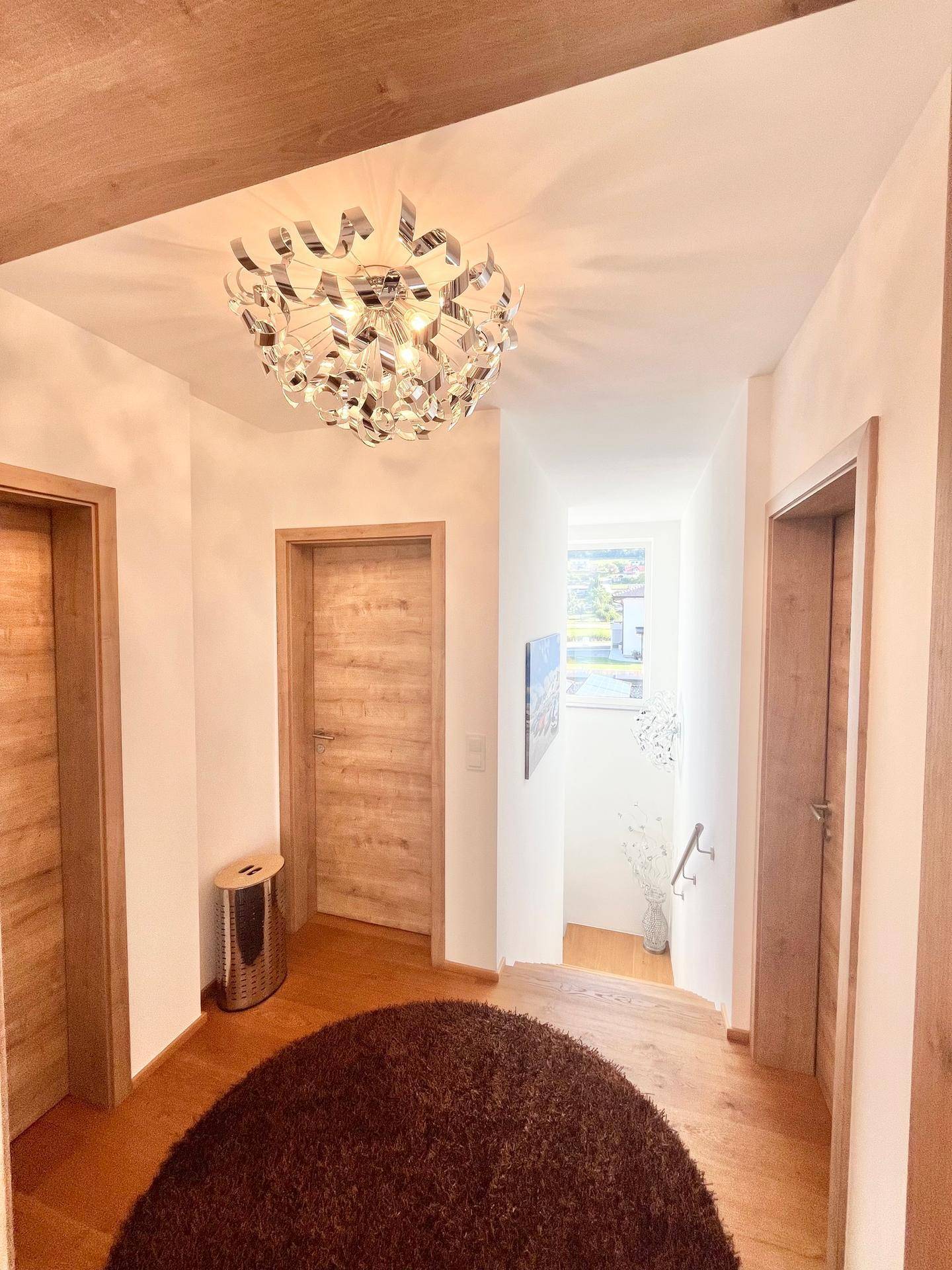 Heller Flur mit Holzboden, modernen Holztüren und einer auffälligen Deckenleuchte.