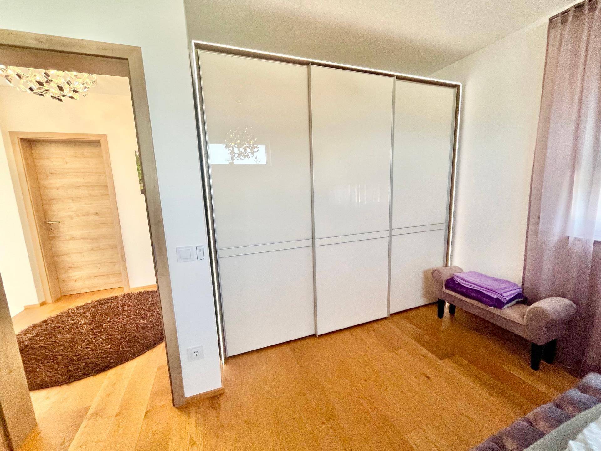 Schlafzimmer mit Einbauschränken, Holzboden und Zugang zu weiteren Räumen.