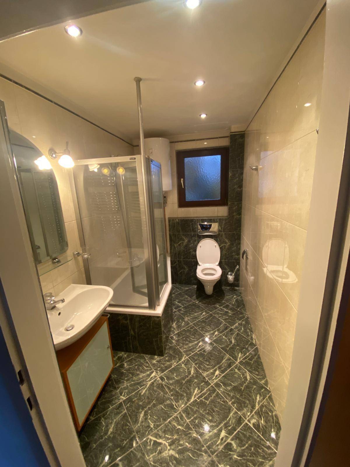 Badezimmer mit dunklen Marmorfliesen, Dusche, WC und Fenster für natürliche Belüftung.