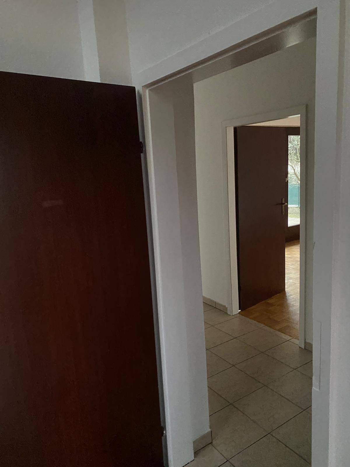 Flur mit Fliesenboden und Blick in angrenzende Zimmer, mit dunklen Holztüren.