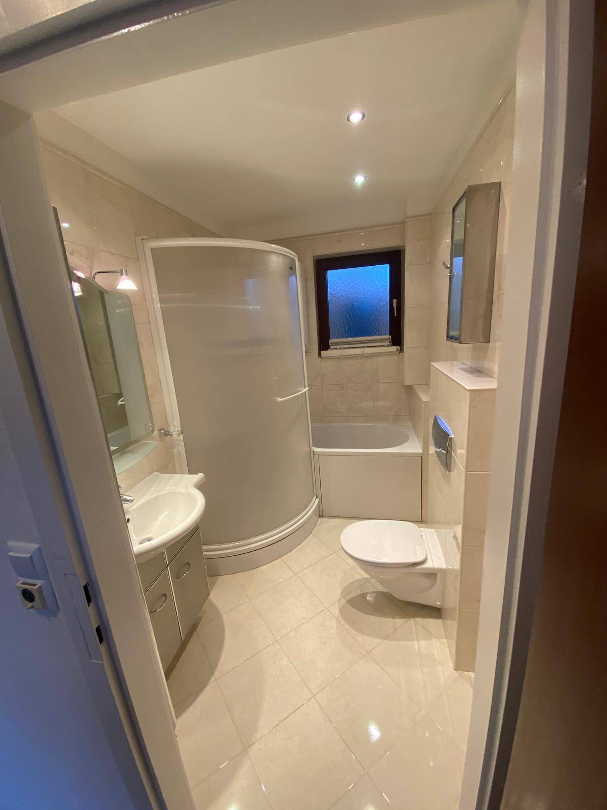 Modernes Badezimmer mit Dusche, Badewanne, WC und Fenster für Tageslicht.