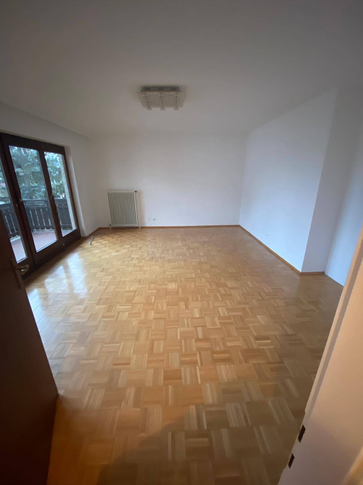 Geräumiges, leeres Zimmer mit Parkettboden und breiter Fensterfront, die viel Licht spendet.