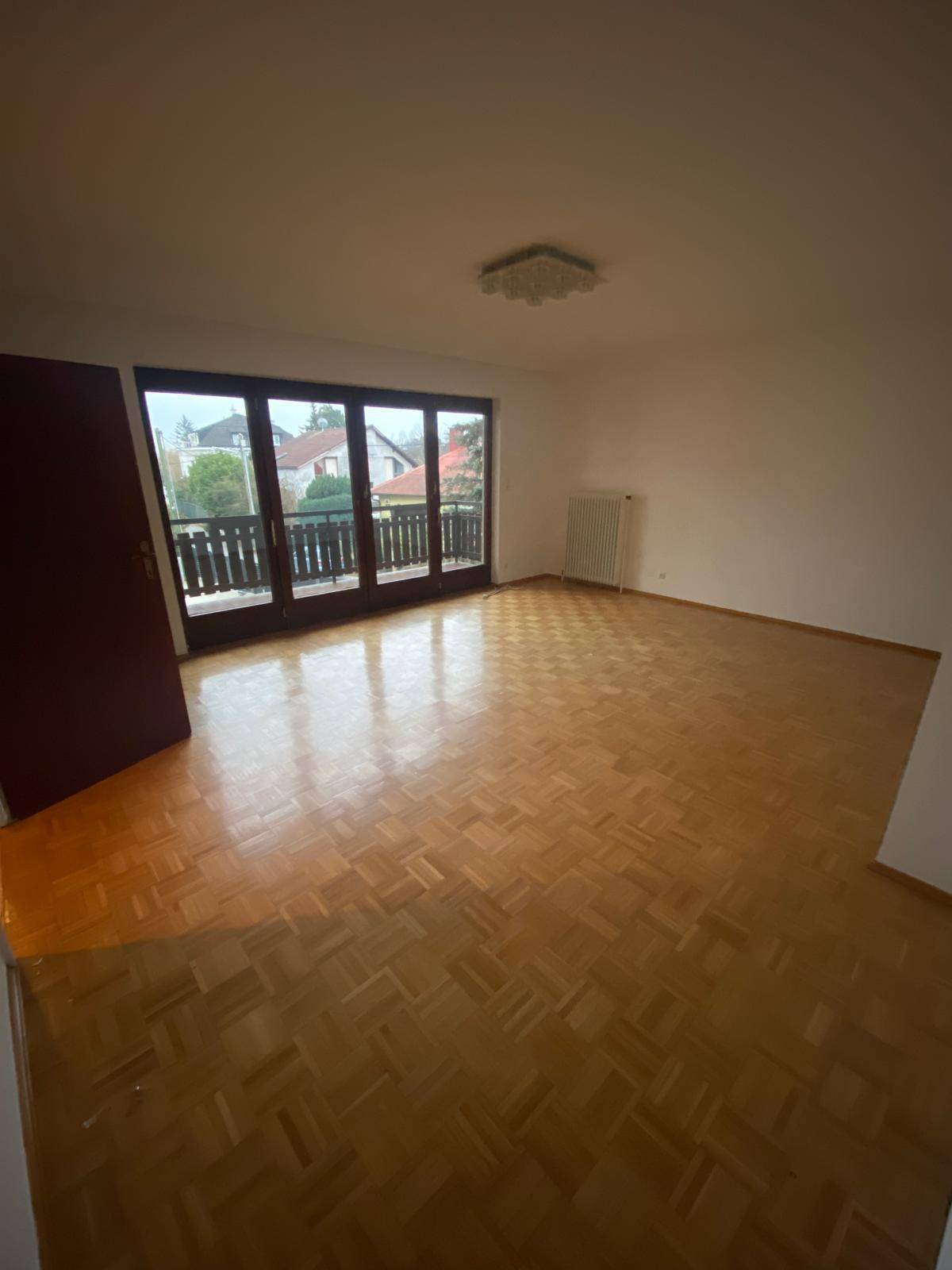 Helles, leeres Zimmer mit Parkettboden und Zugang zu einem großen Balkon.