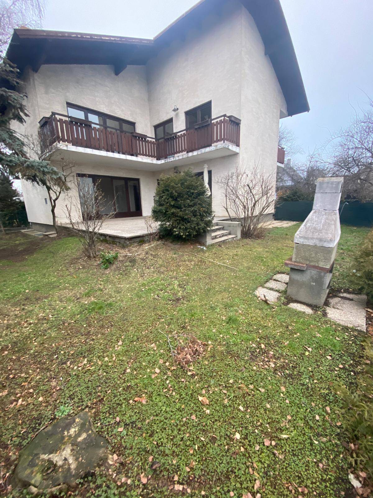 Gartenbereich mit Rasenfläche, Bäumen und einem gemauerten Grillplatz neben dem Haus.