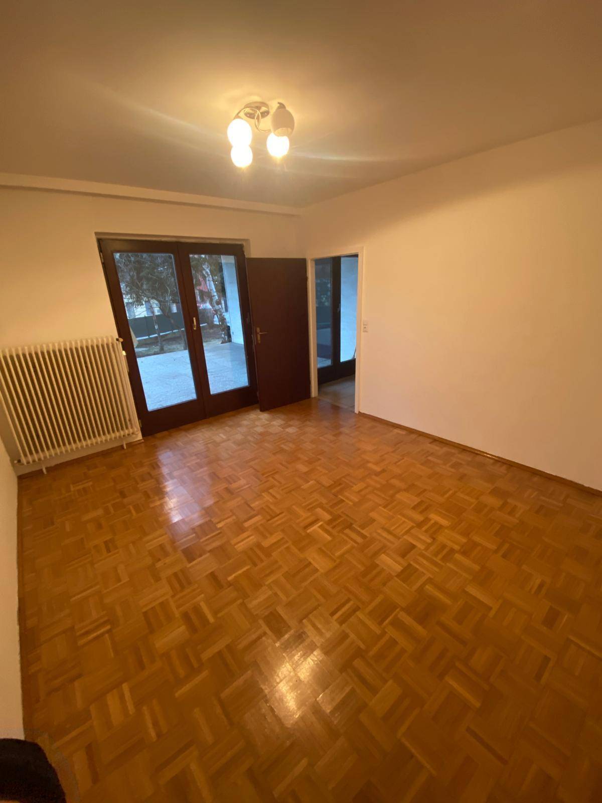 Helles, leeres Zimmer mit Parkettboden und Zugang zu einem großen Balkon.