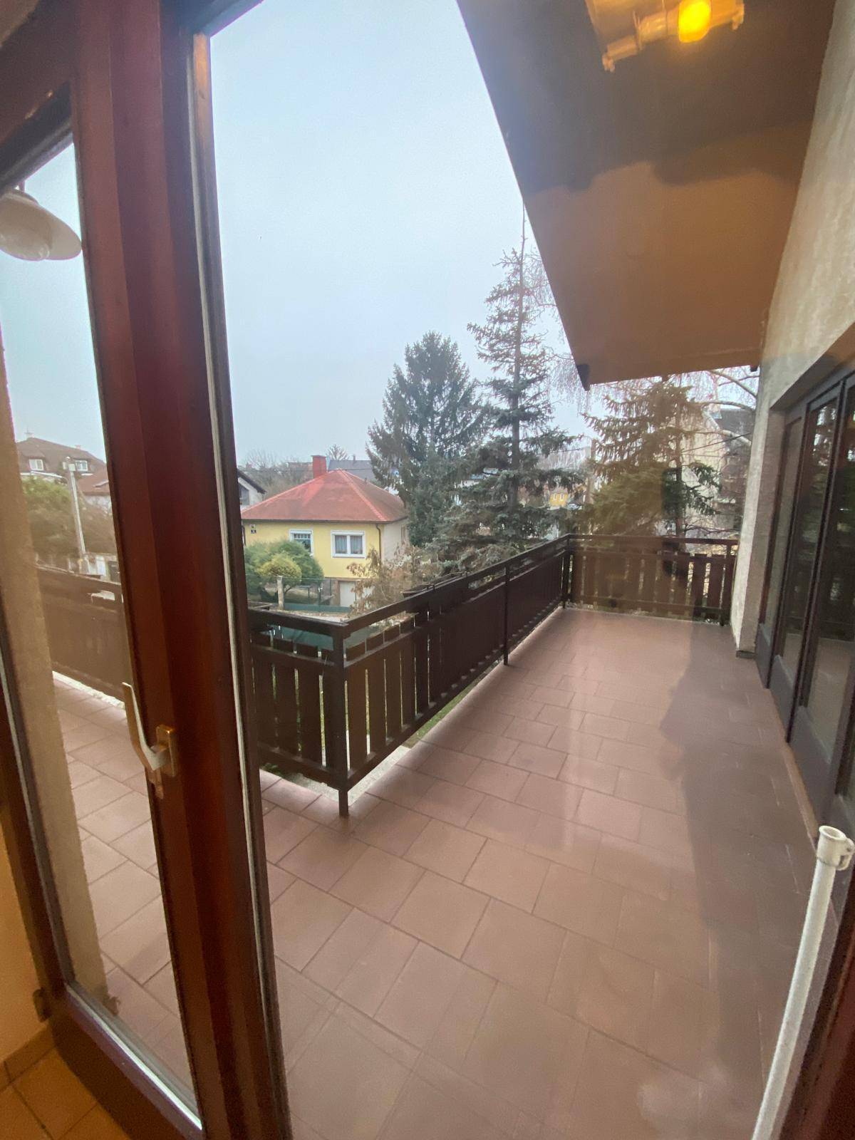 Großer Balkon mit Fliesenboden und Holzgeländer, bietet Blick auf die Umgebung.