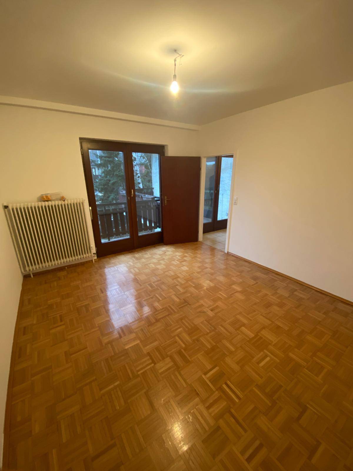 Helles, leeres Zimmer mit Parkettboden und Zugang zu einem Balkon.