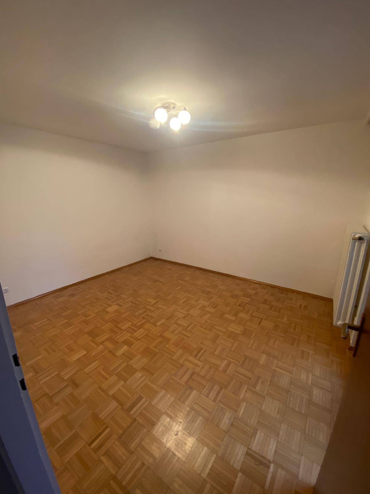 Geräumiges, leeres Zimmer mit Parkettboden und breiter Fensterfront, die viel Licht spendet.