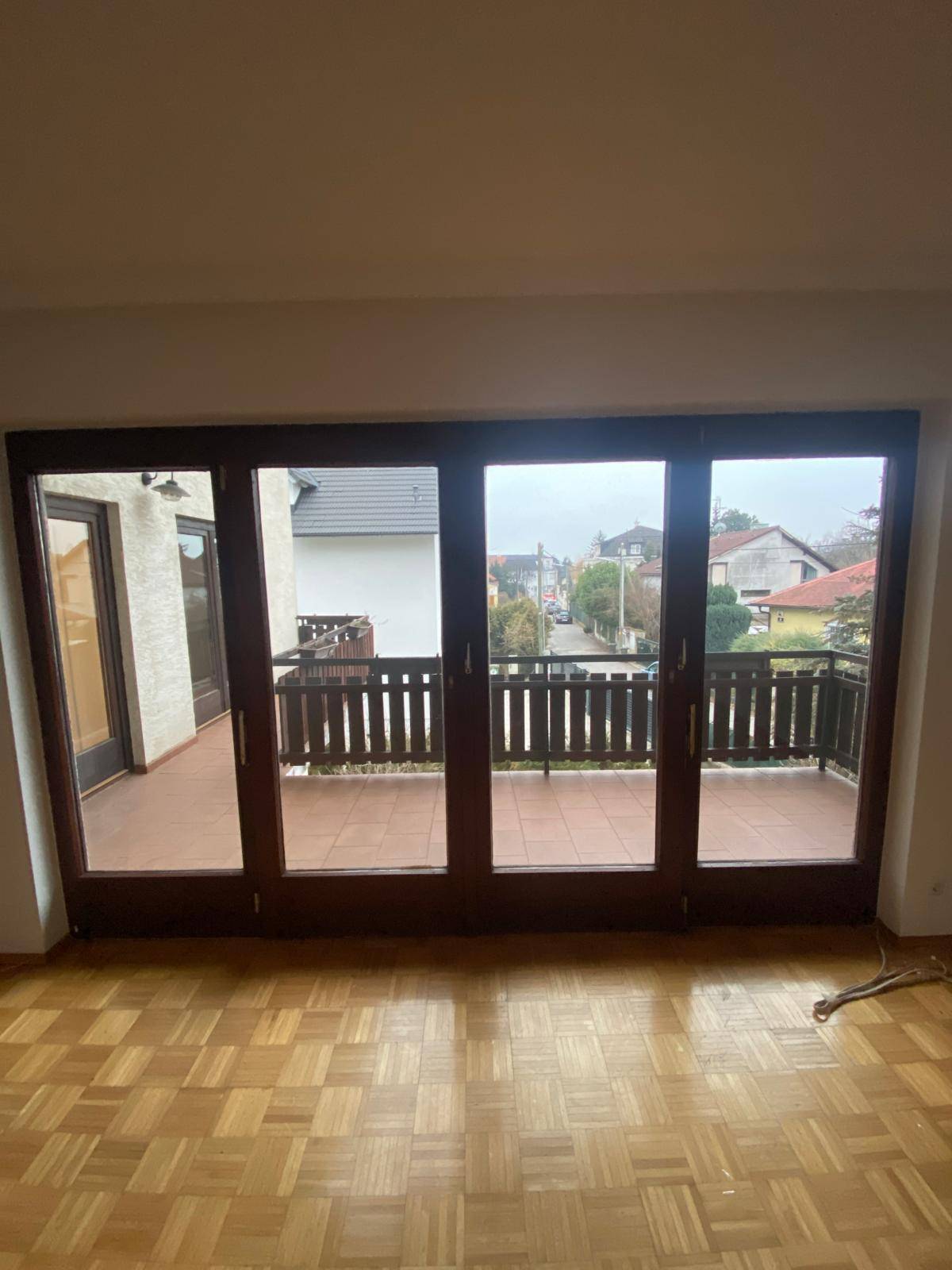 Geräumiges Zimmer mit Parkettboden und breiter Fensterfront zum Balkon.