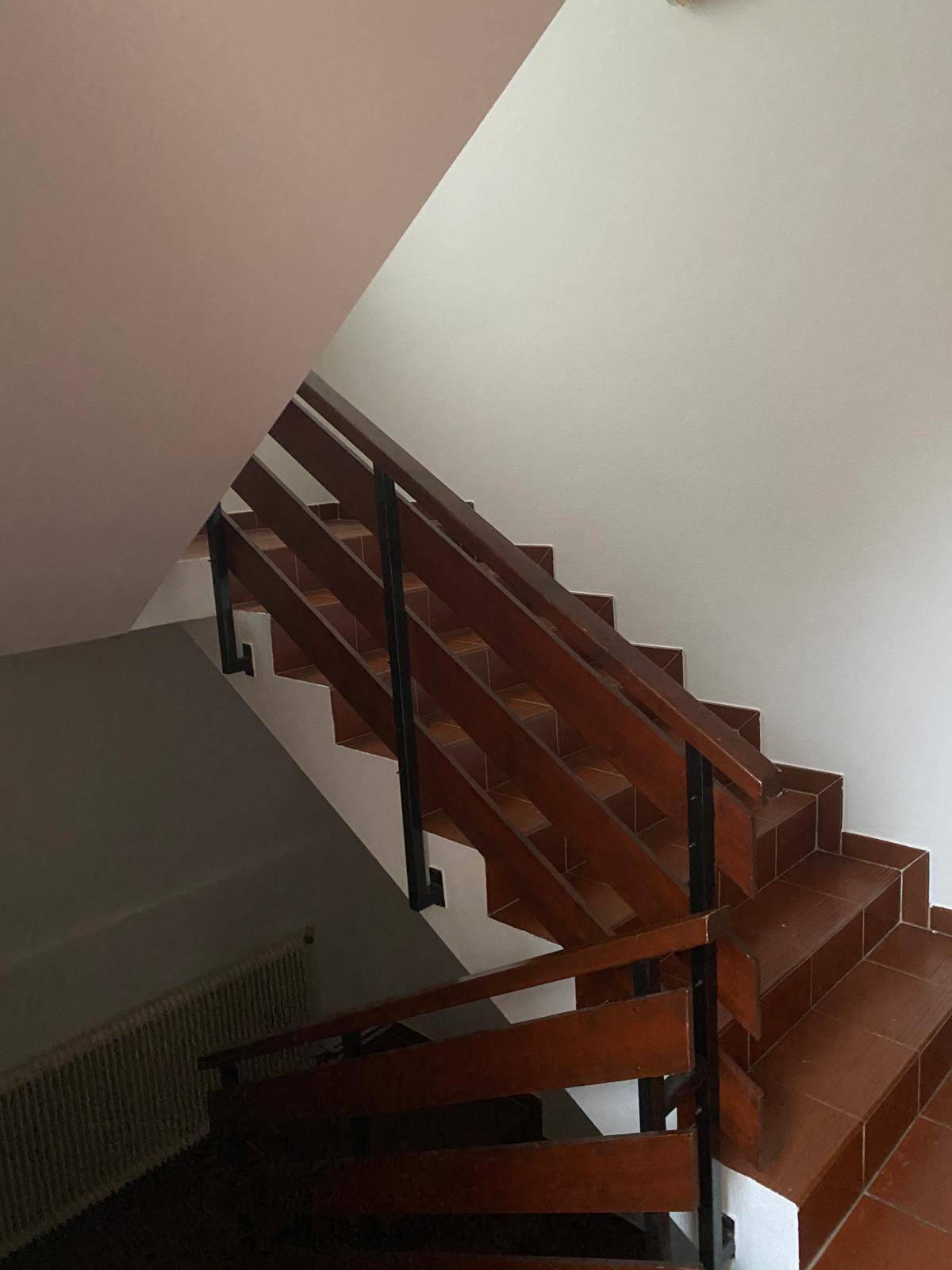 Treppenhaus mit Holzgeländer und braunen Fliesenstufen, das die Stockwerke verbindet.
