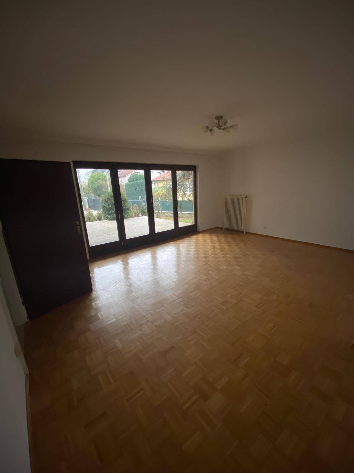 Helles, leeres Zimmer mit Parkettboden und Zugang zu einer großen Terrasse.