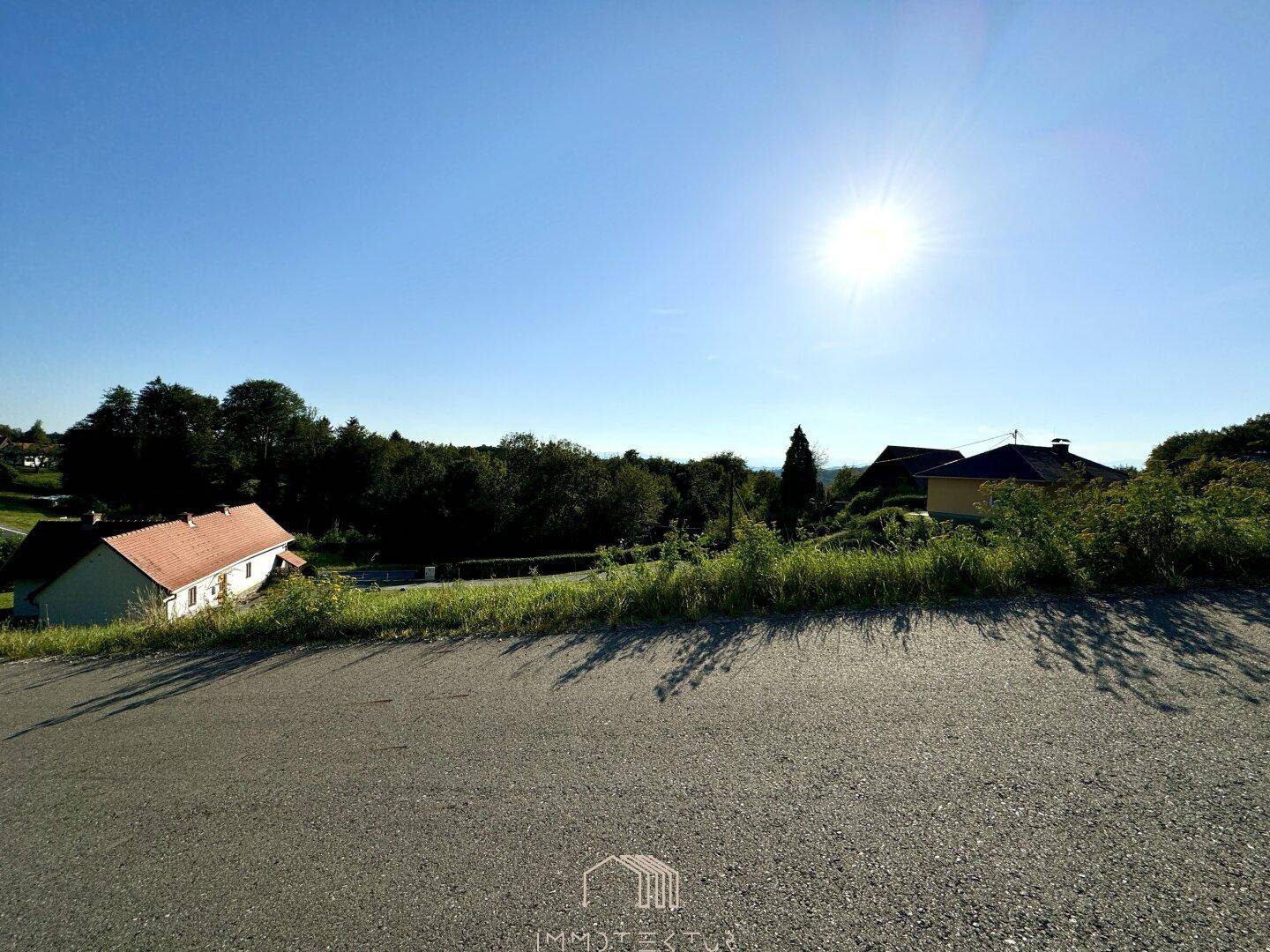 Sonnige Aussicht auf die grüne Landschaft mit Feldern und Häusern in der Ferne unter strahlendem Himmel.