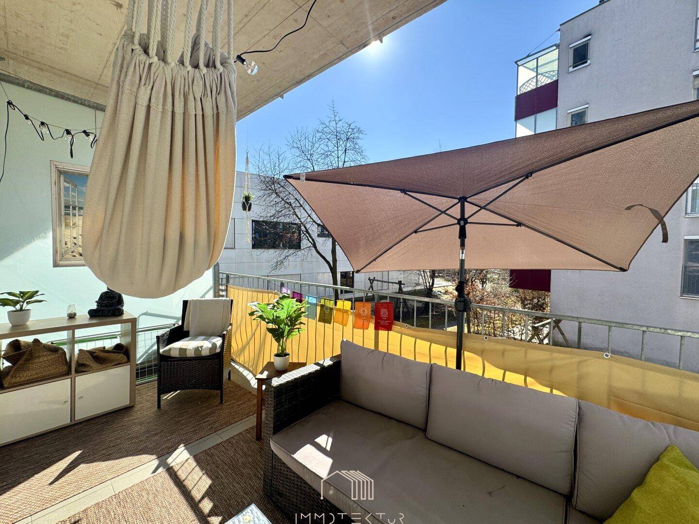 Heller Balkon mit Hängesessel, Sonnenschirm und bequemen Sitzmöbeln für entspannte Stunden im Freien.