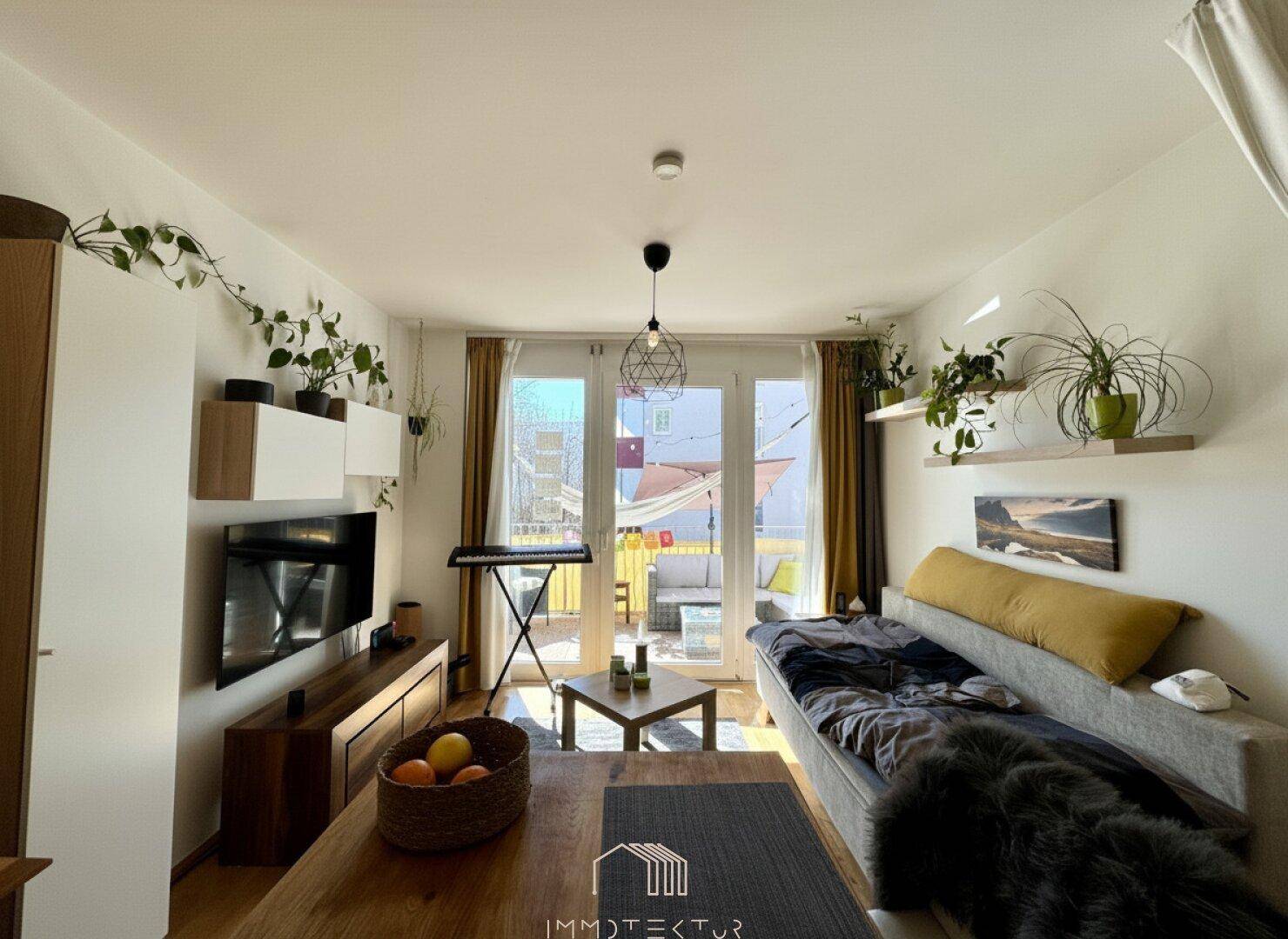 Heller Wohnbereich mit Sofa, Holzboden und großen Fenstern zum Balkon.