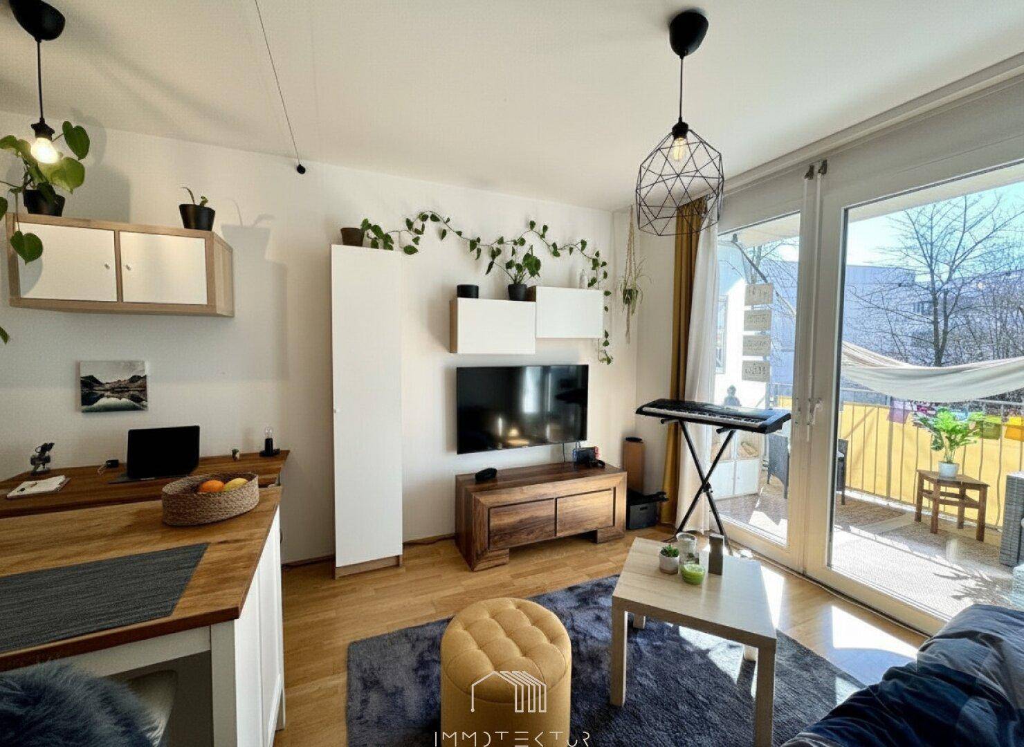 Gemütlicher Wohnbereich mit Holzboden, Fernseher und Zugang zum sonnigen Balkon.