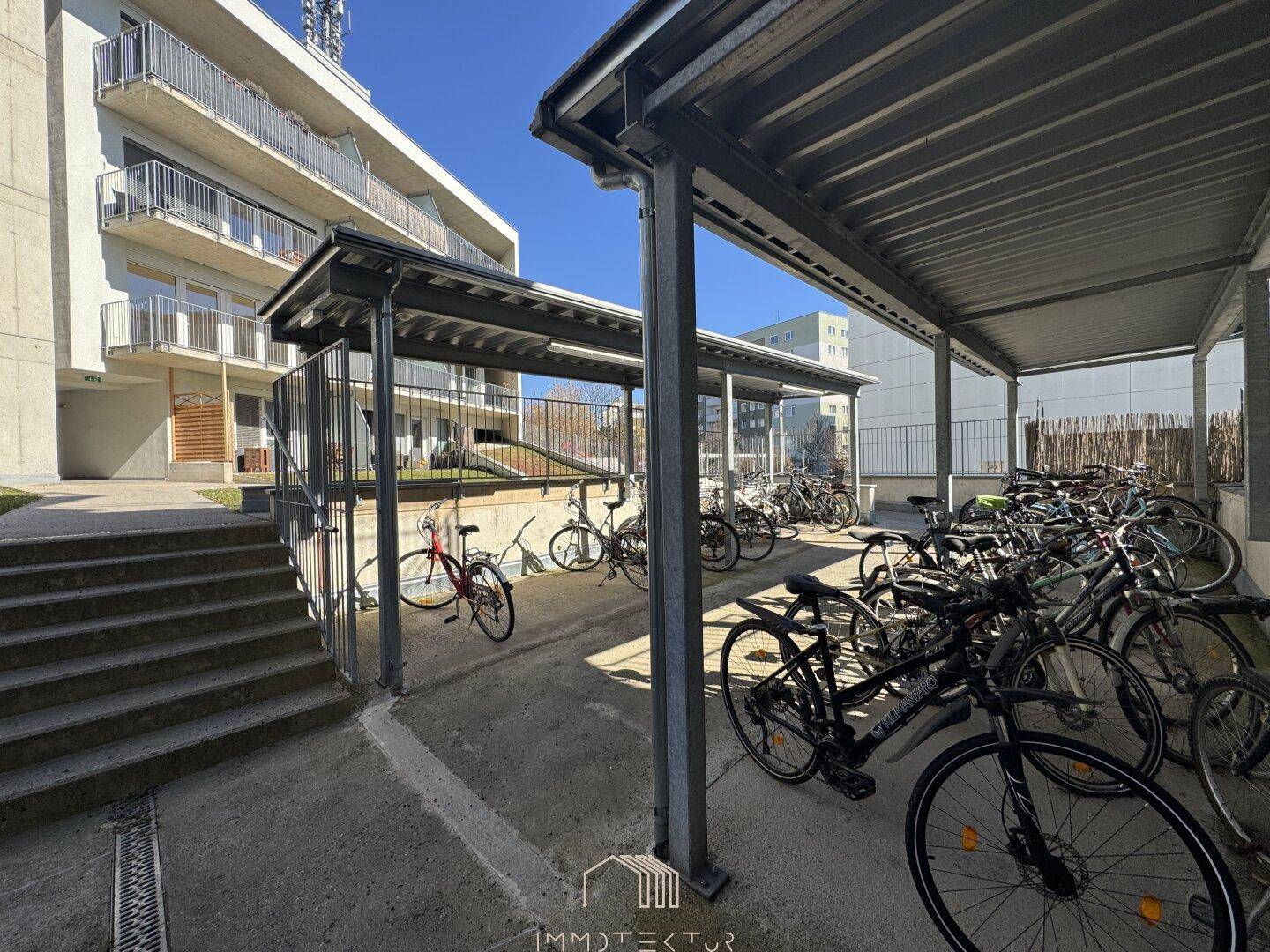 Überdachter Fahrradabstellplatz vor einem modernen Wohngebäude.