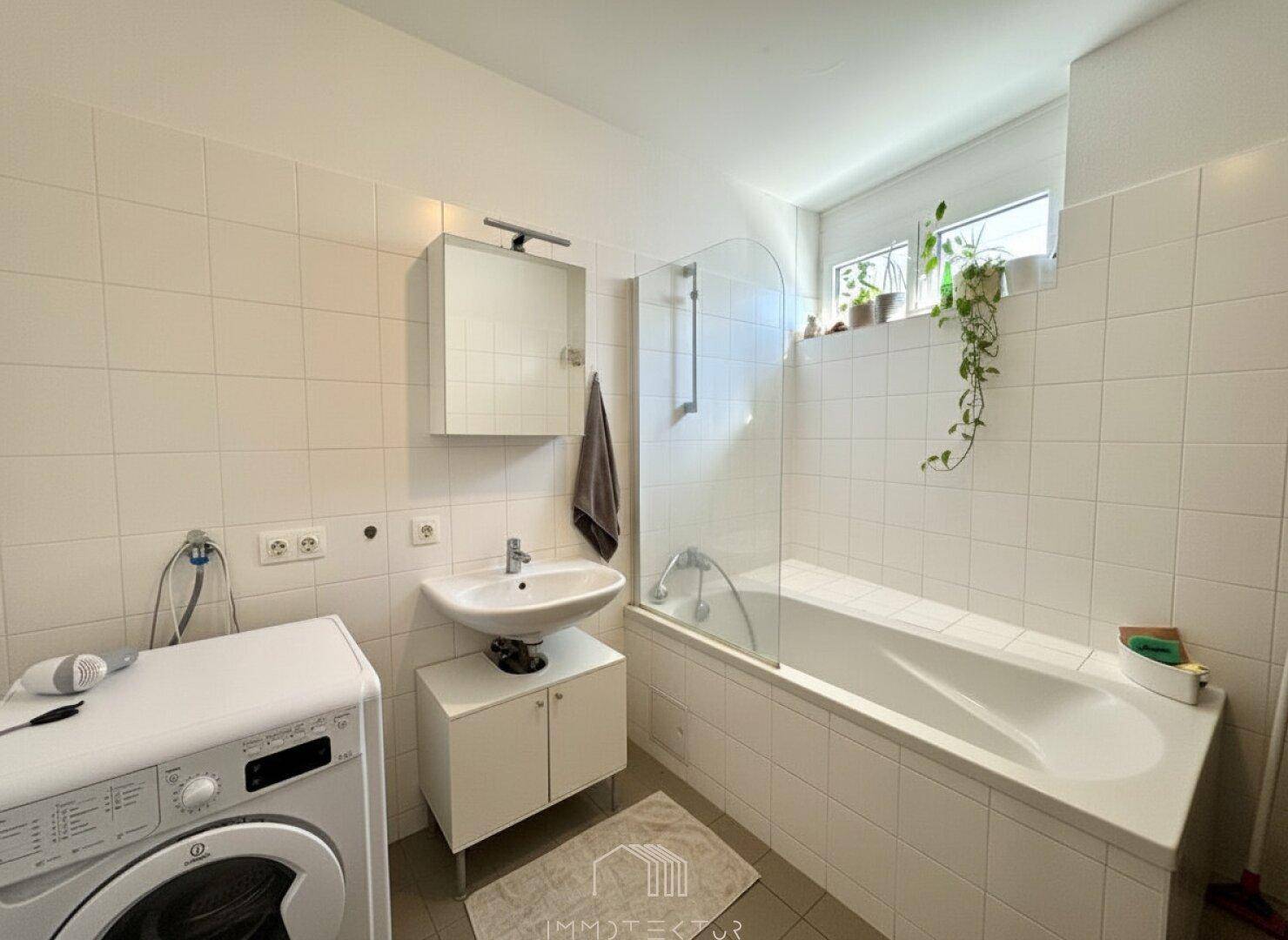 Badezimmer mit Badewanne, Waschbecken und Platz für eine Waschmaschine.