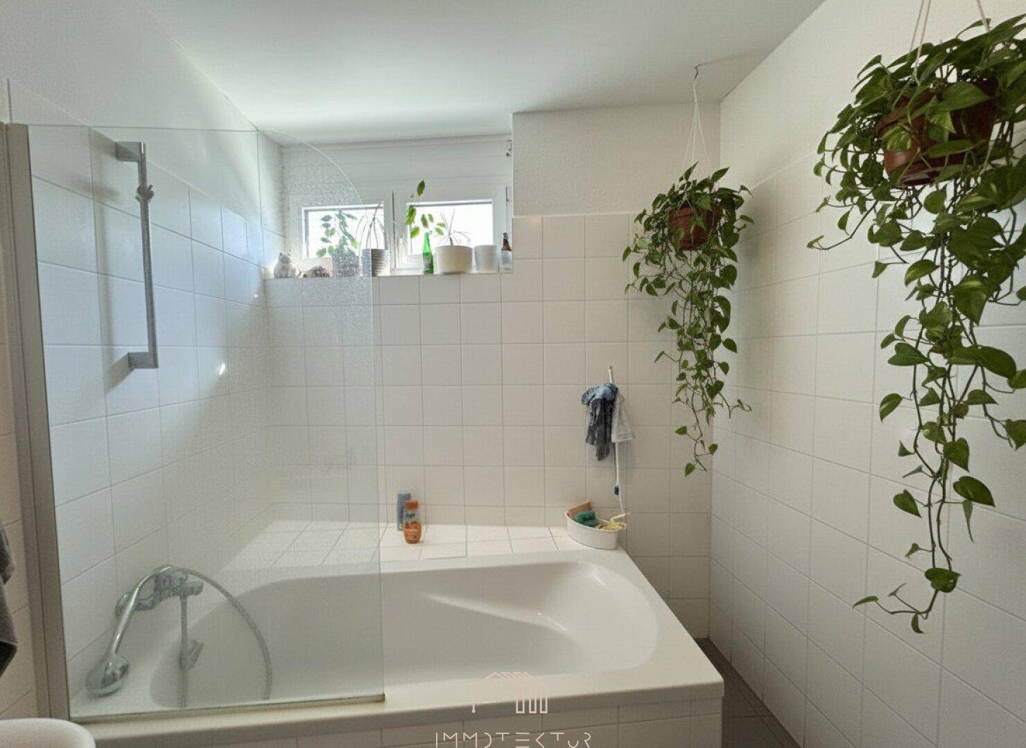 Helles Badezimmer mit Badewanne und Duschmöglichkeit hinter einer Glaswand.