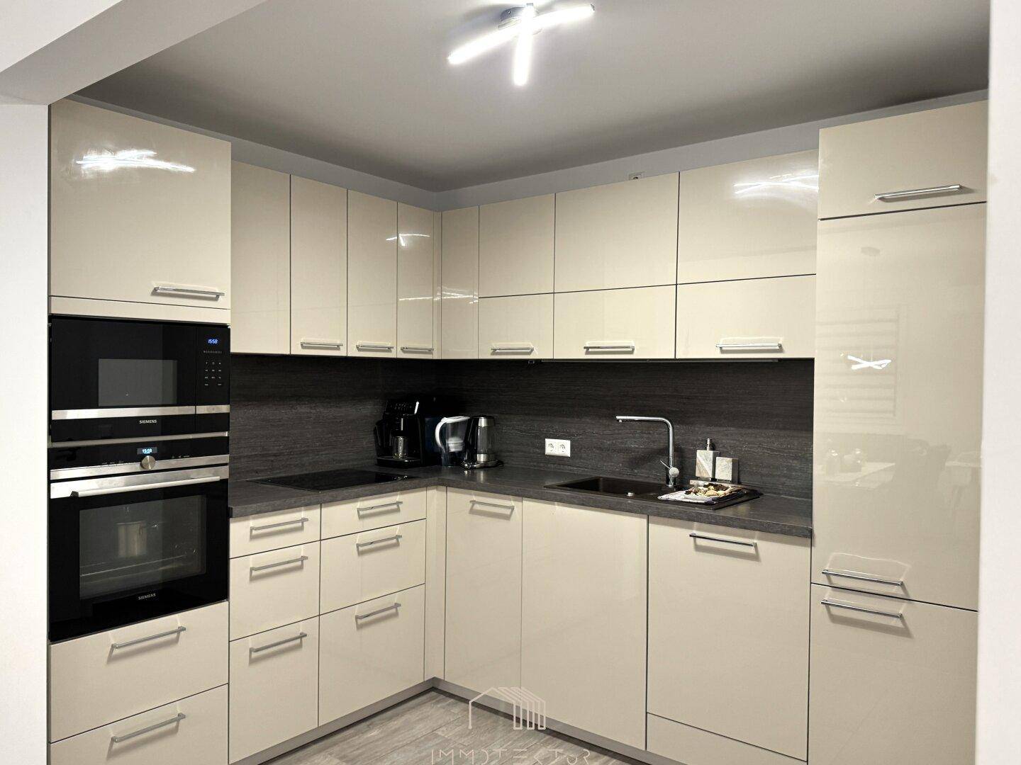 Eckansicht der modernen Küche mit beigen Hochglanzfronten und hochwertigen Einbaugeräten.