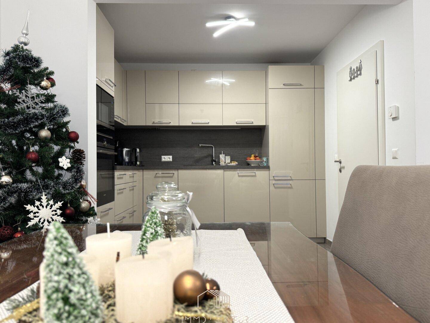 Moderne Küche mit beigen Hochglanzfronten, integrierten Geräten und festlicher Weihnachtsdekoration.