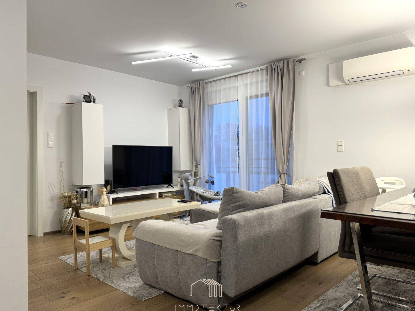 Heller Wohnbereich mit Sofa, Fernseher, Holzboden und Klimaanlage an der Wand.