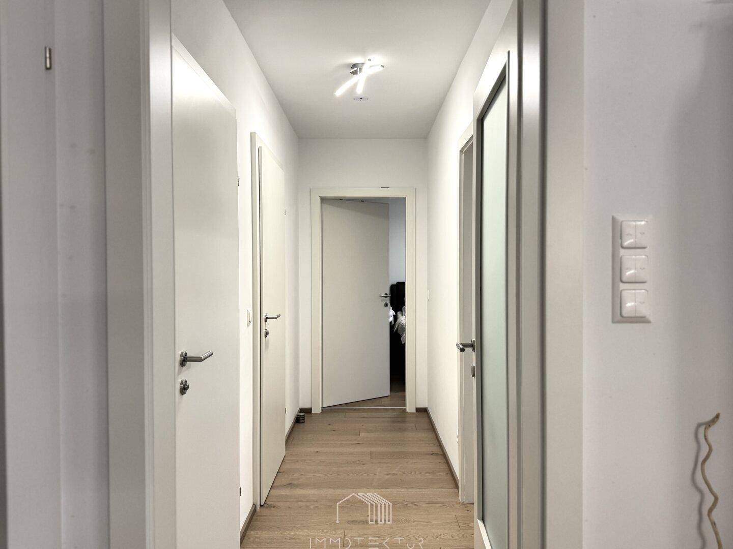 Heller Flur mit Holzboden und weißen Wänden, der zu verschiedenen Zimmern führt.