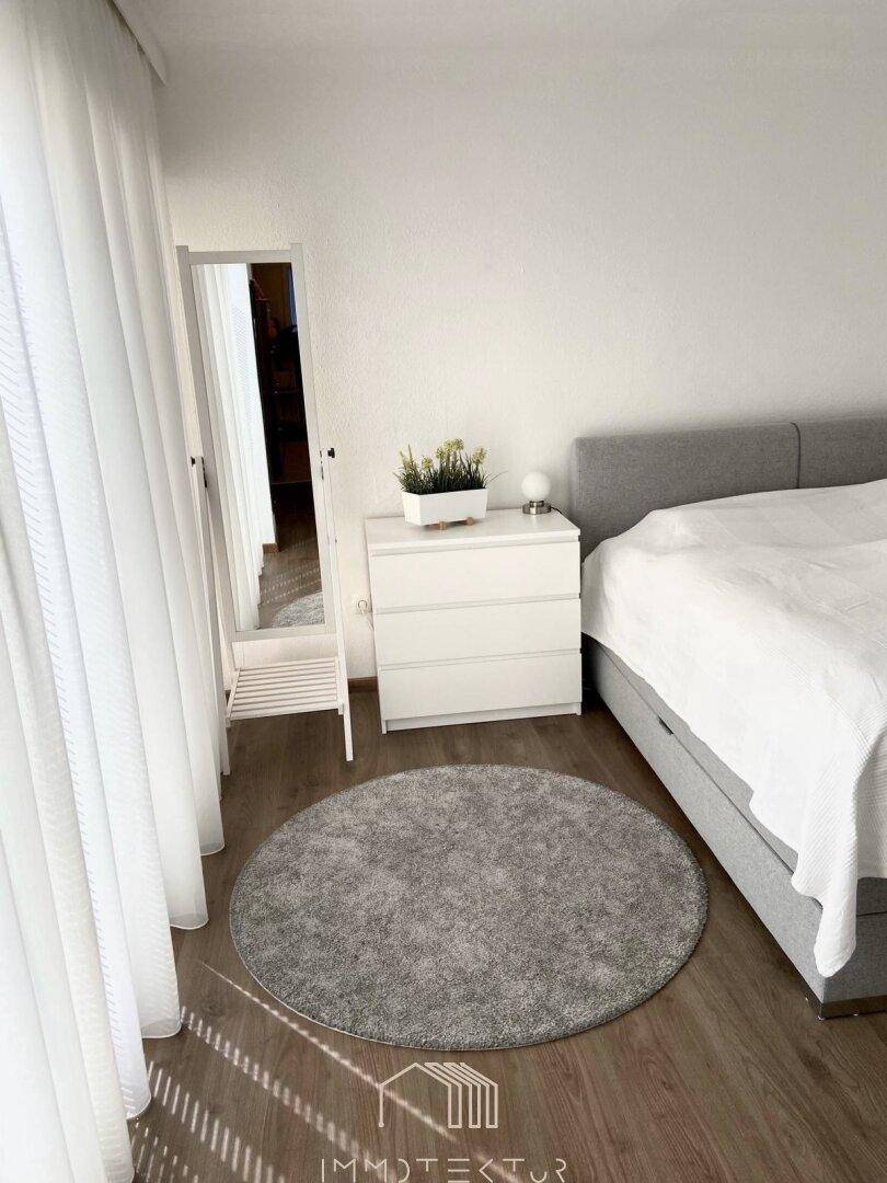 Helles Schlafzimmer mit Doppelbett, Nachttisch und großem Spiegel.