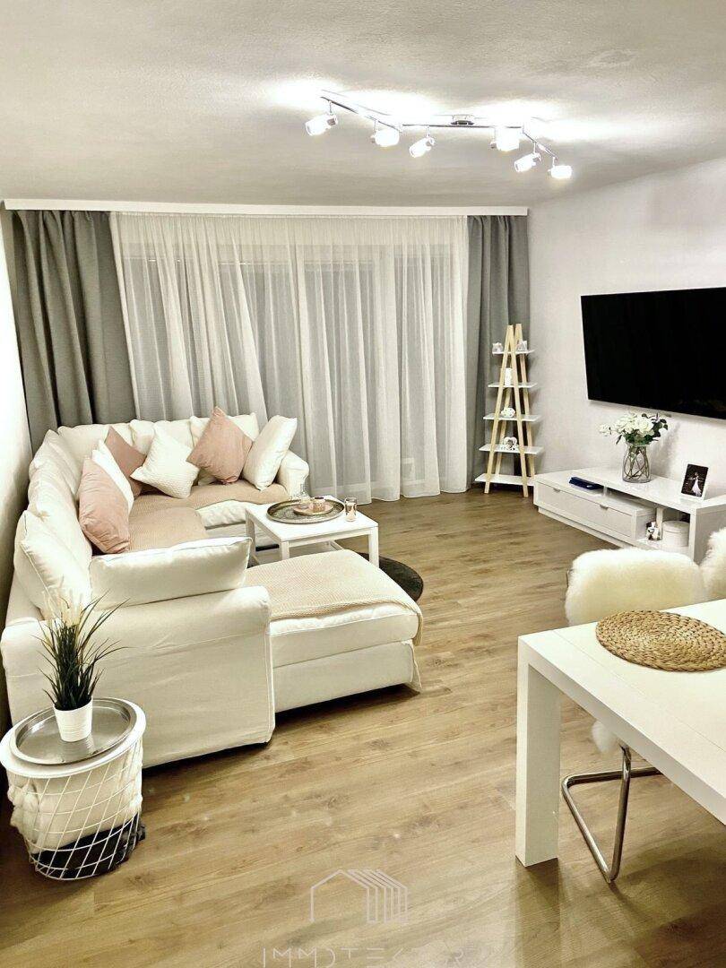 Helles Wohnzimmer mit beigem Ecksofa, Holzboden und modernem TV-Bereich.