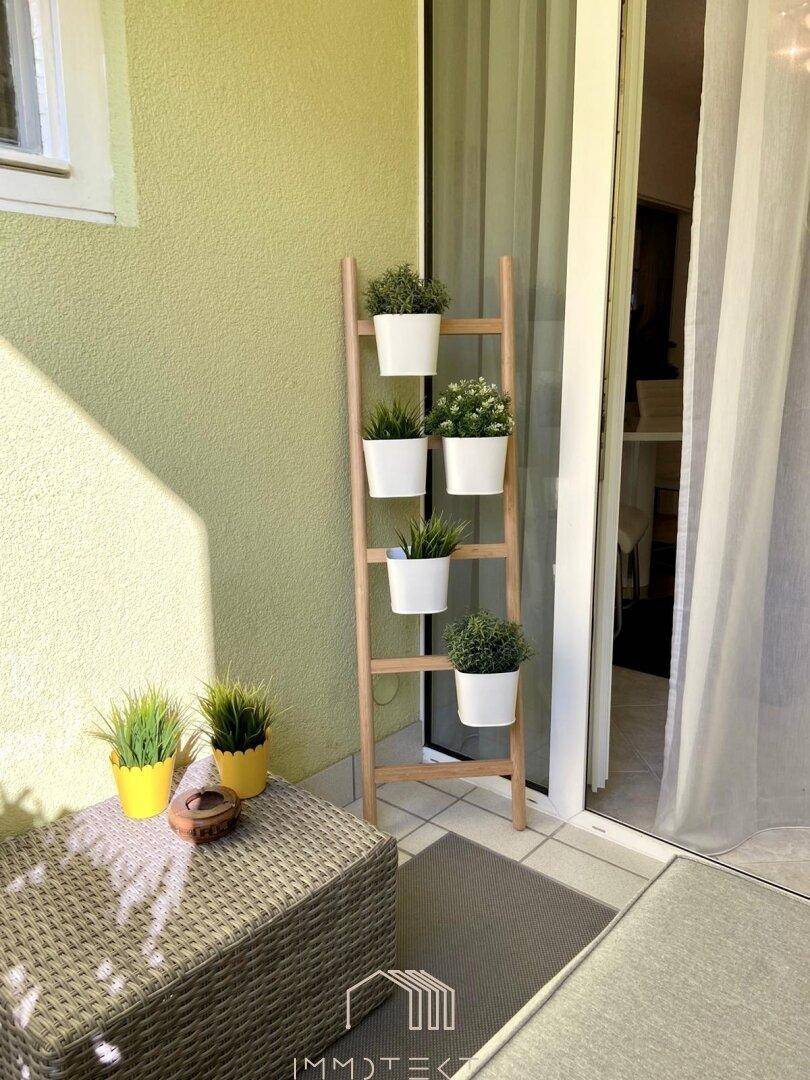 Kleiner Balkon mit Pflanzenleiter und Sitzgelegenheit, ideal für Entspannung im Freien.