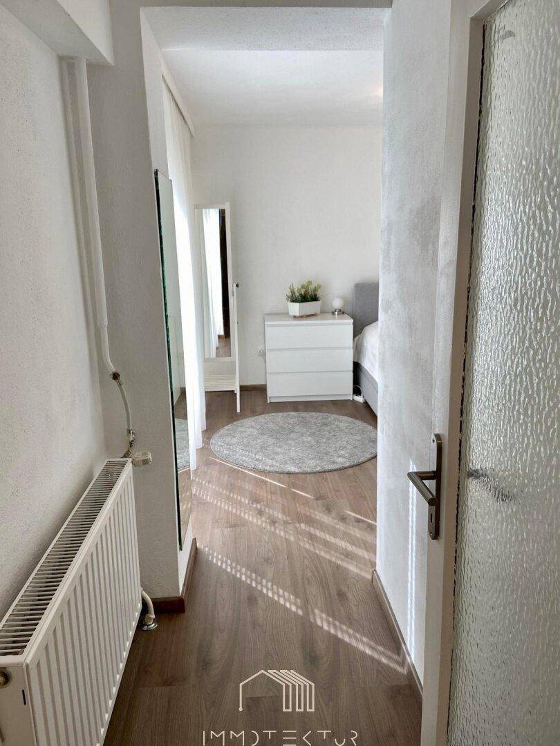 Flur mit Heizkörper und Blick in ein helles Schlafzimmer.