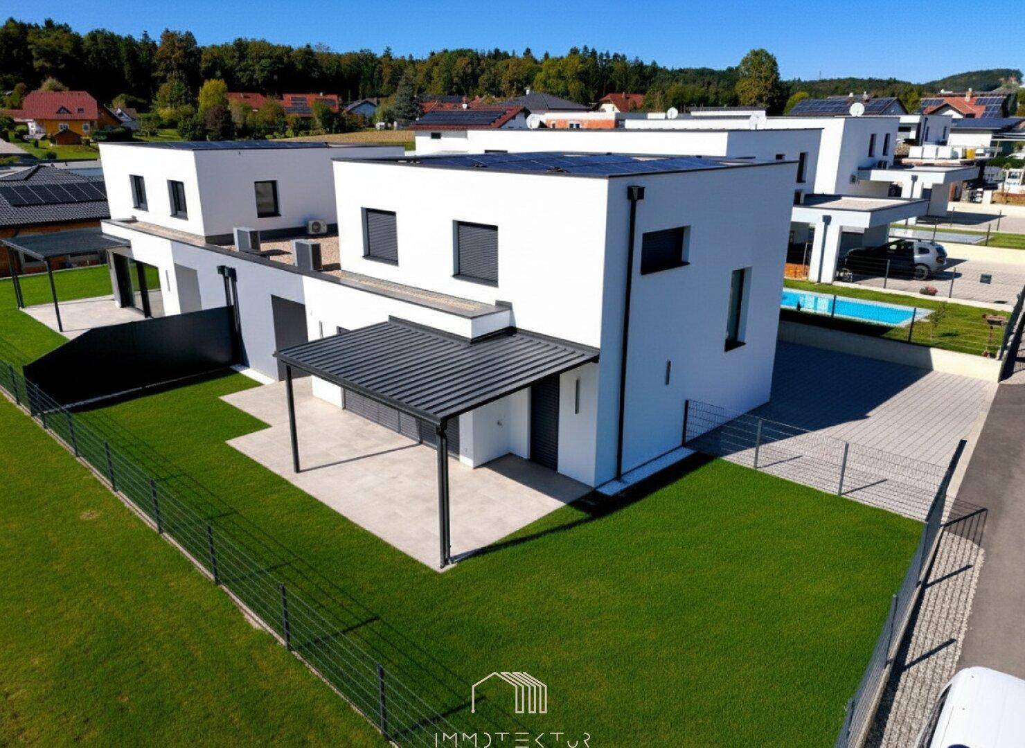 Luftaufnahme einer modernen Wohnsiedlung mit mehreren Häusern, Gärten und einem Pool.