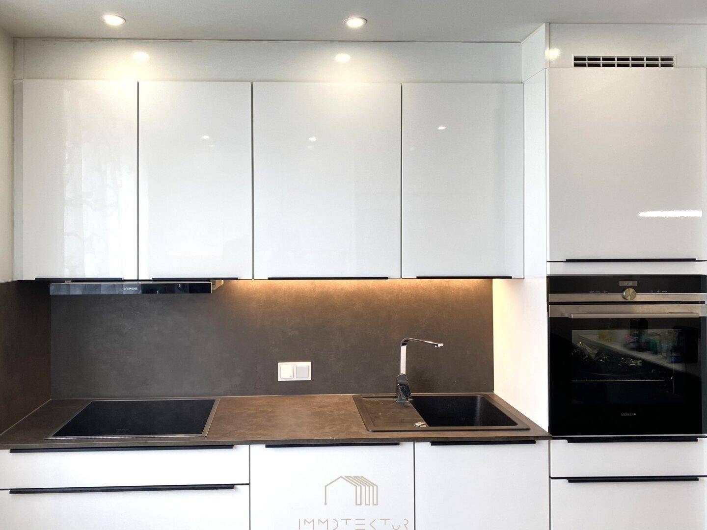 Moderne Einbauküche mit weißen Hochglanzfronten, Induktionskochfeld und Backofen.