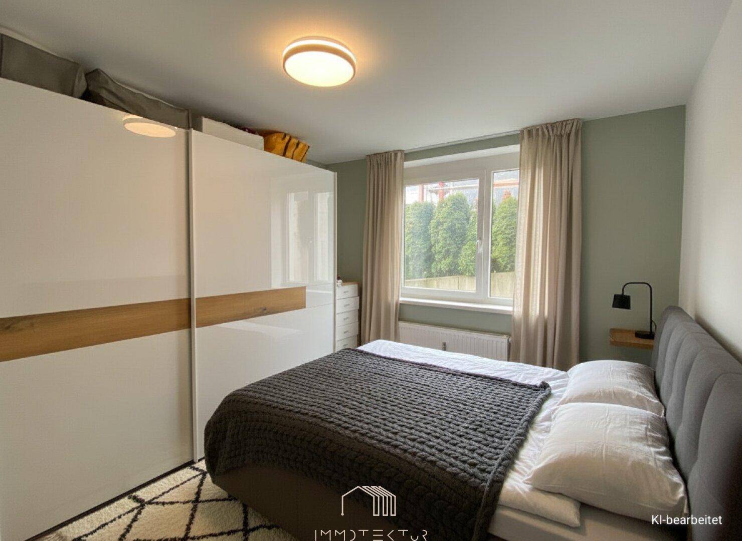 Helles Schlafzimmer mit großem Bett, Einbauschrank und Fenster mit Blick ins Grüne.