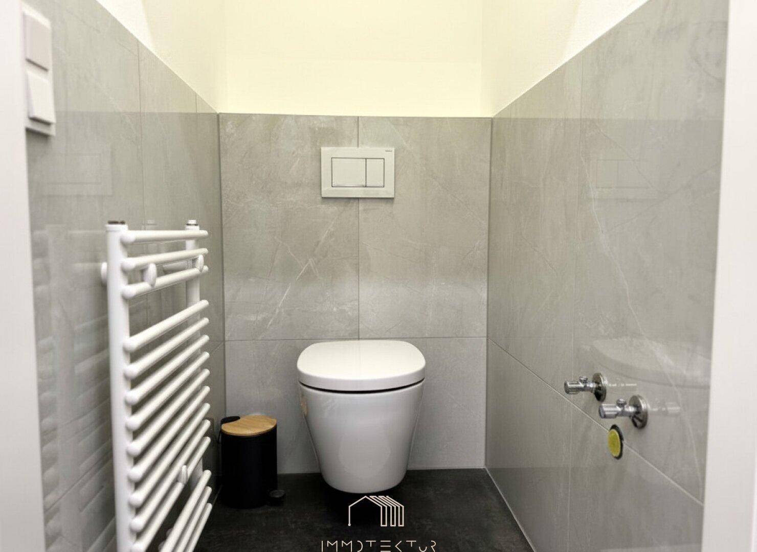 Modernes Gäste-WC mit wandhängender Toilette, Heizkörper und hellgrauen Fliesen.