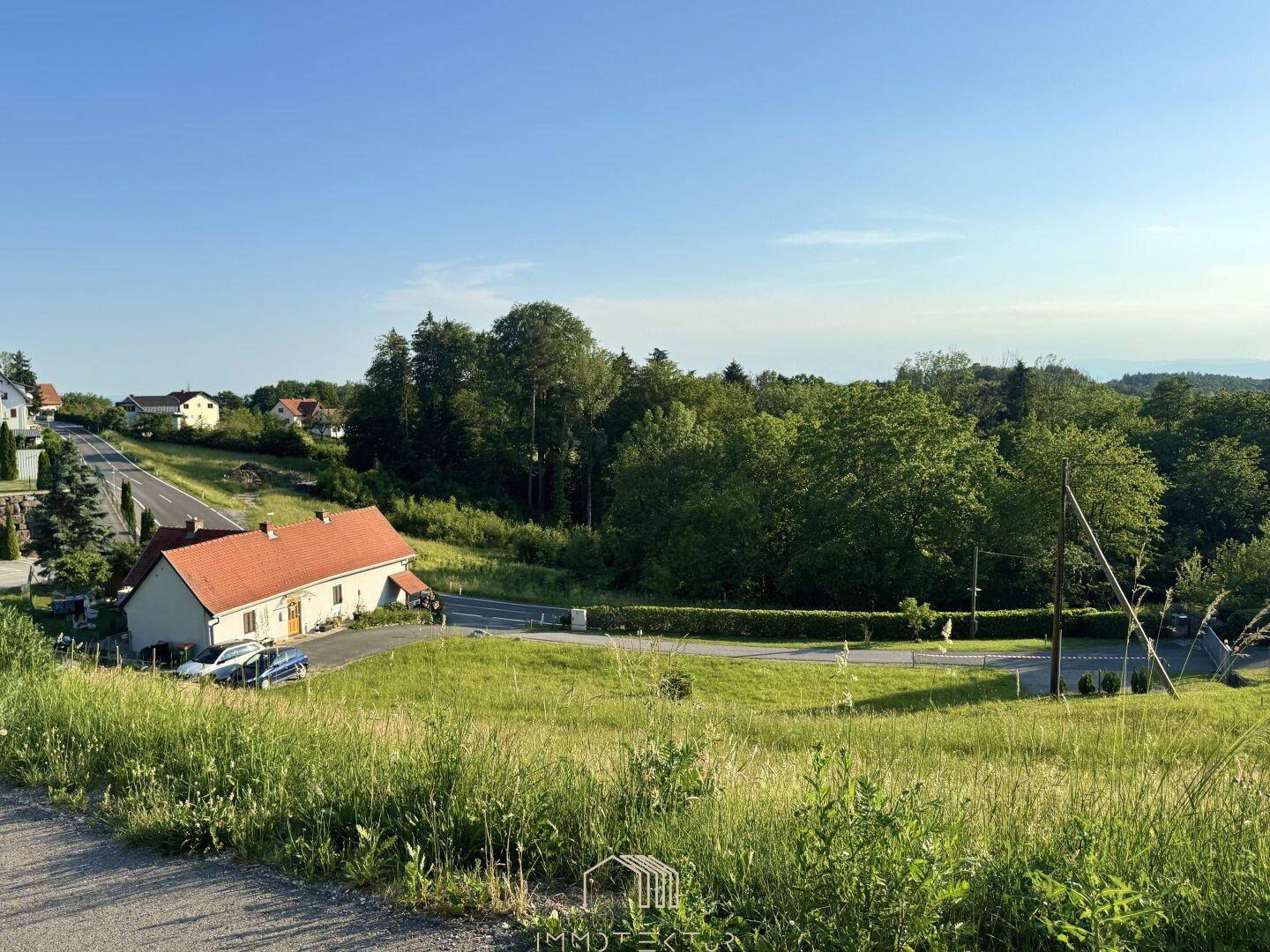 Panoramablick auf eine ländliche Gegend mit Häusern, einer Straße und üppiger grüner Vegetation.