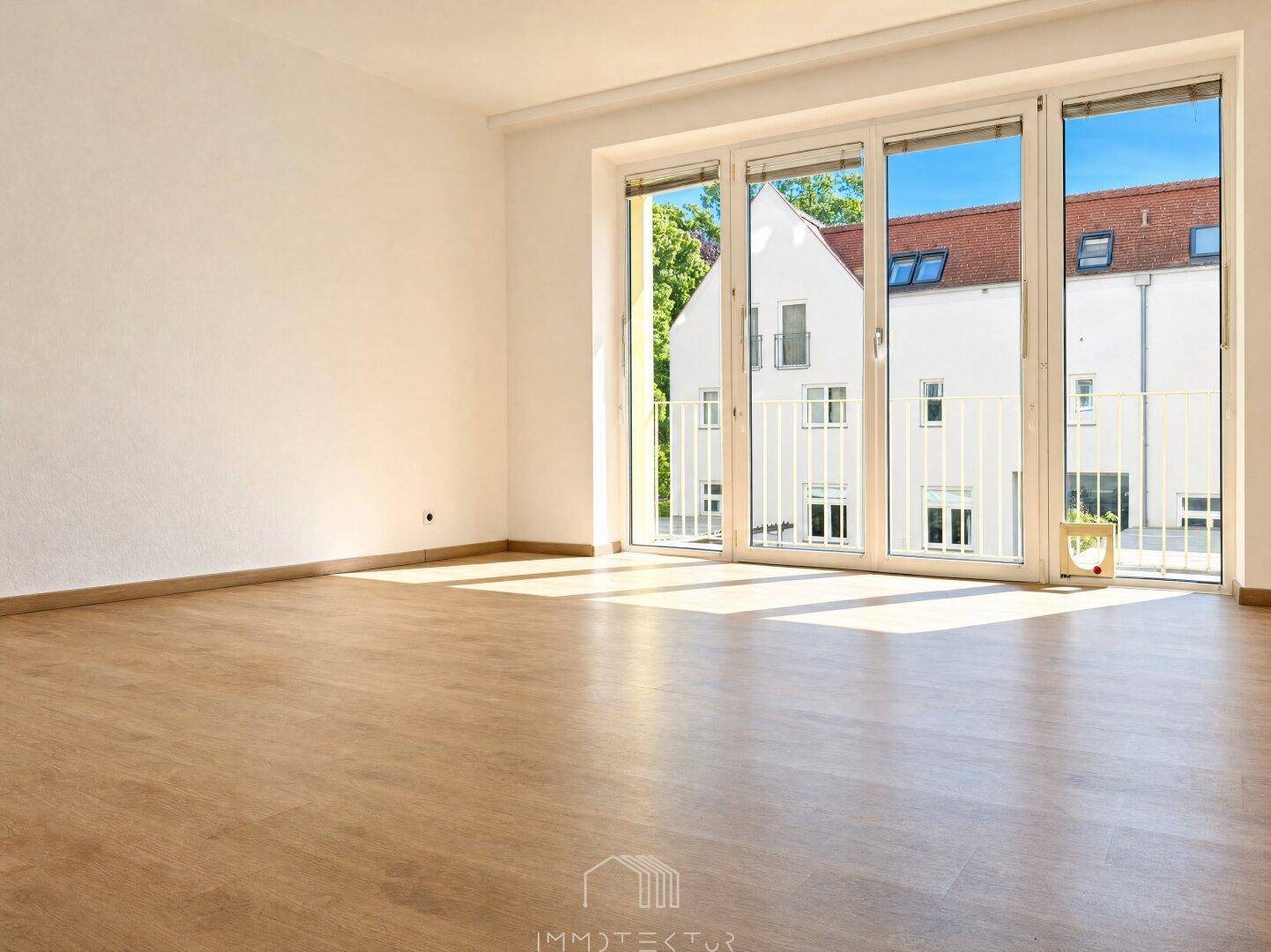 Lichtdurchfluteter Wohnbereich mit Laminatboden und großen Fenstern mit Blick auf die Nachbarschaft.