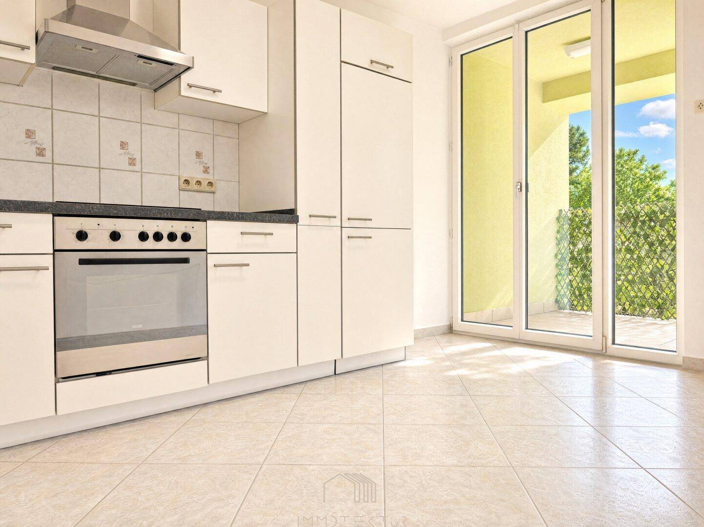 Helle Küche mit weißen Schränken, Fliesenboden und Zugang zu einem Balkon.
