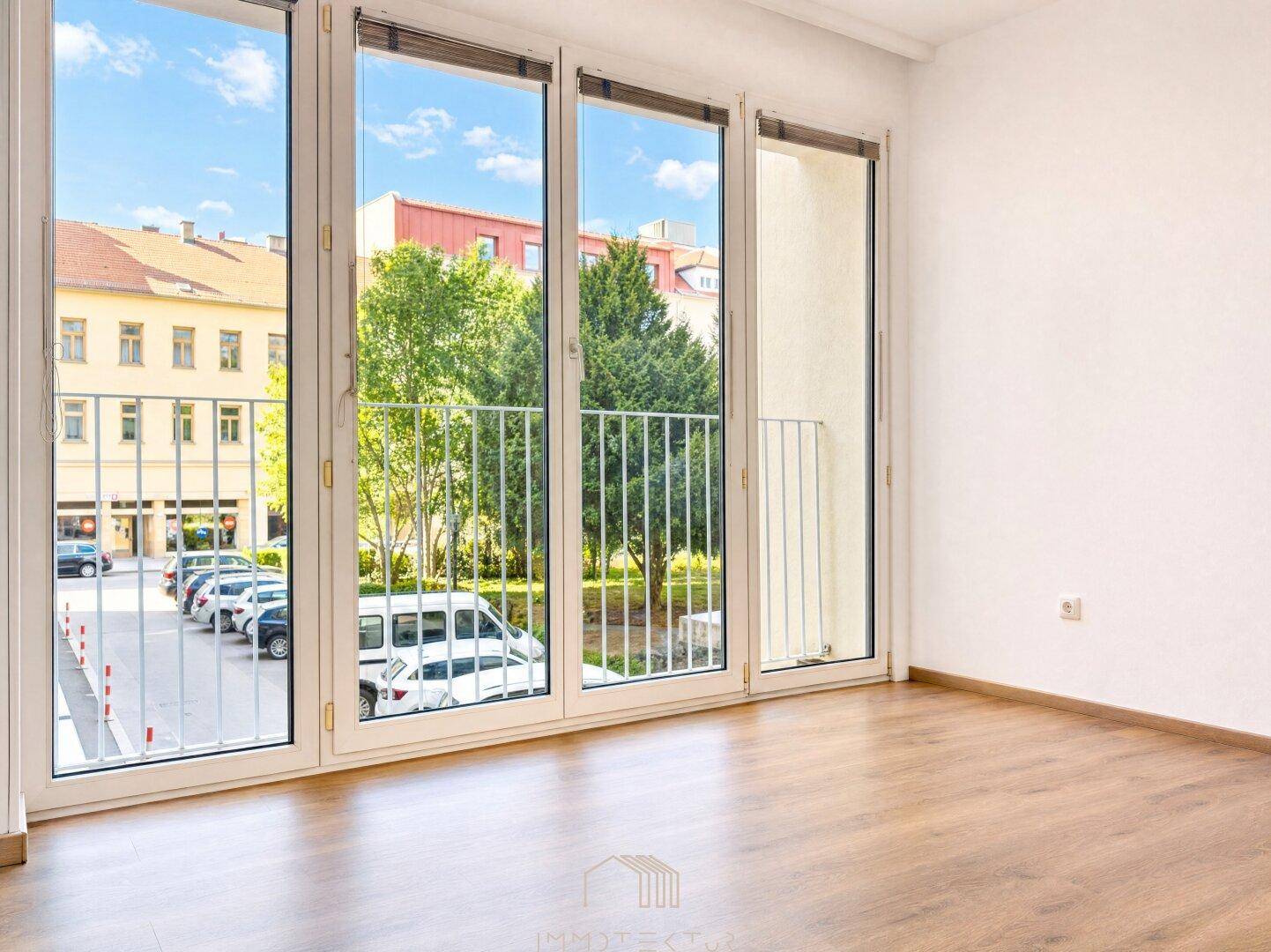 Geräumiges Zimmer mit Laminatboden und großen Fenstern, die einen Blick auf die Straße bieten.