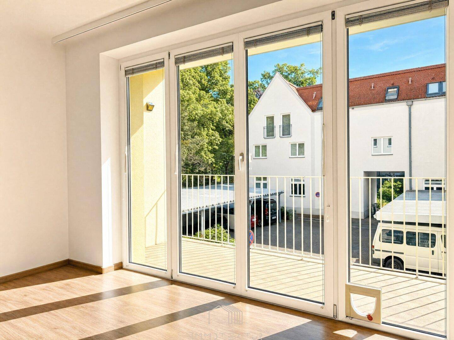 Heller Wohnraum mit Laminatboden und großen Fenstern, die einen Blick auf den Innenhof ermöglichen.