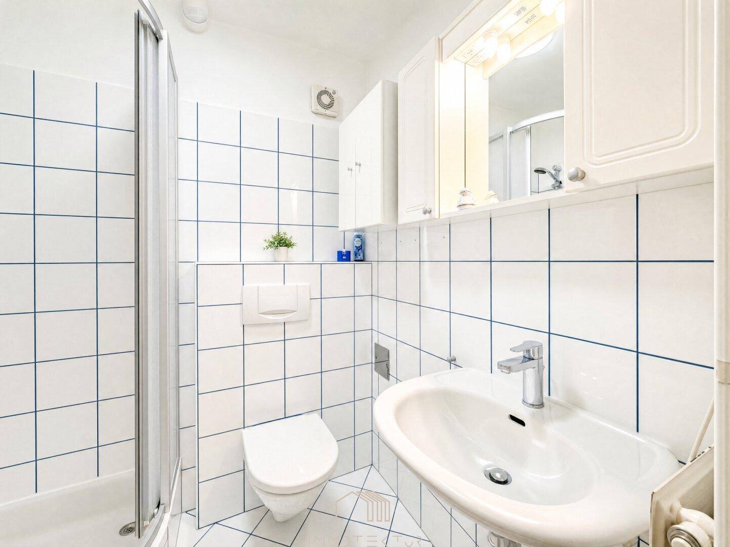 Modernes Badezimmer mit weißen Fliesen, Dusche, WC und Waschbecken.