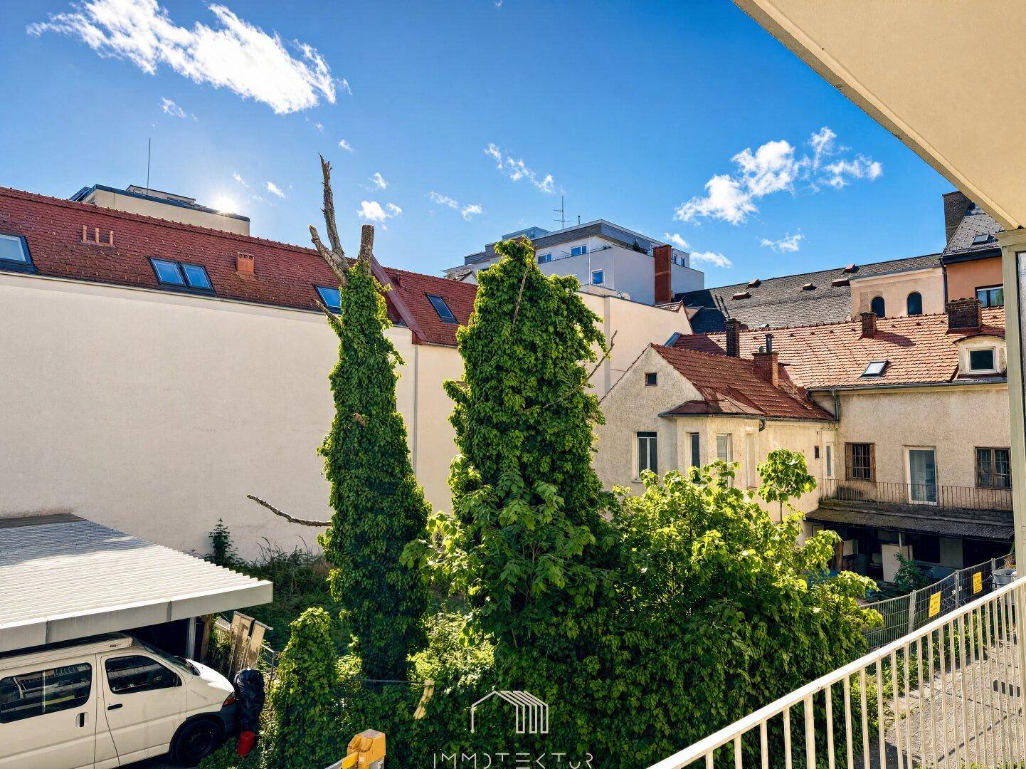 Balkon mit Blick auf die umliegenden Gebäude und Bäume unter einem blauen Himmel.