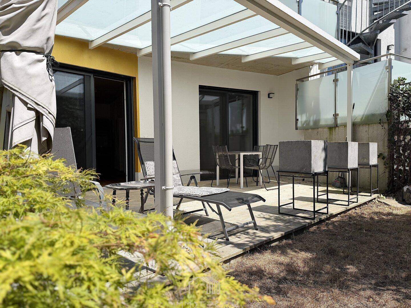 Überdachte Terrasse mit Gartenmöbeln und Zugang zu einem kleinen Gartenbereich.