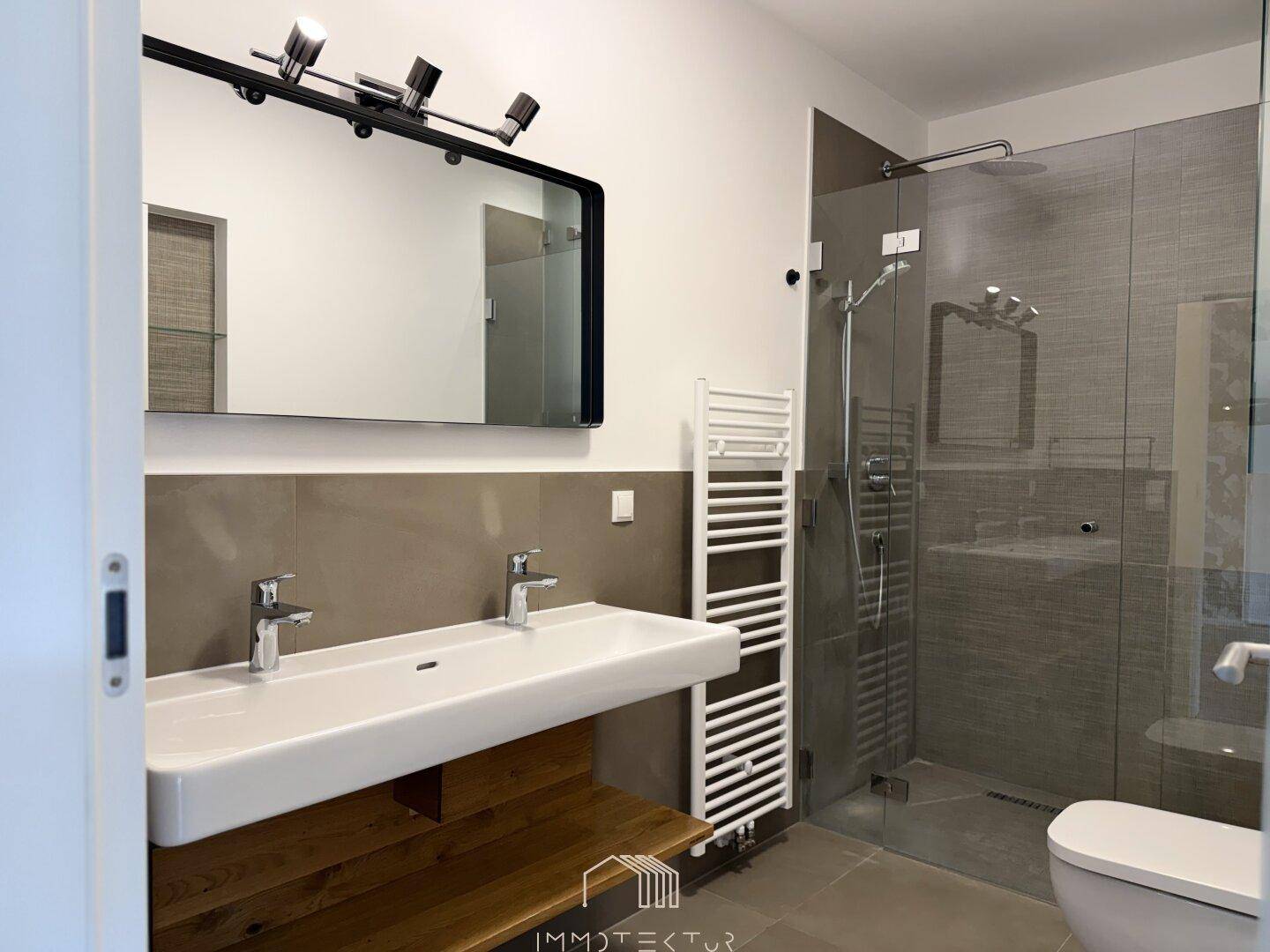 Modernes Badezimmer mit Doppelwaschbecken, großer begehbarer Dusche und beheiztem Handtuchhalter.