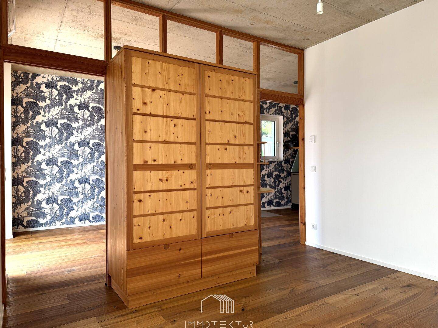 Geräumiger Raum mit Holzboden, Sichtbetondecke und einem großen Holzschrank.