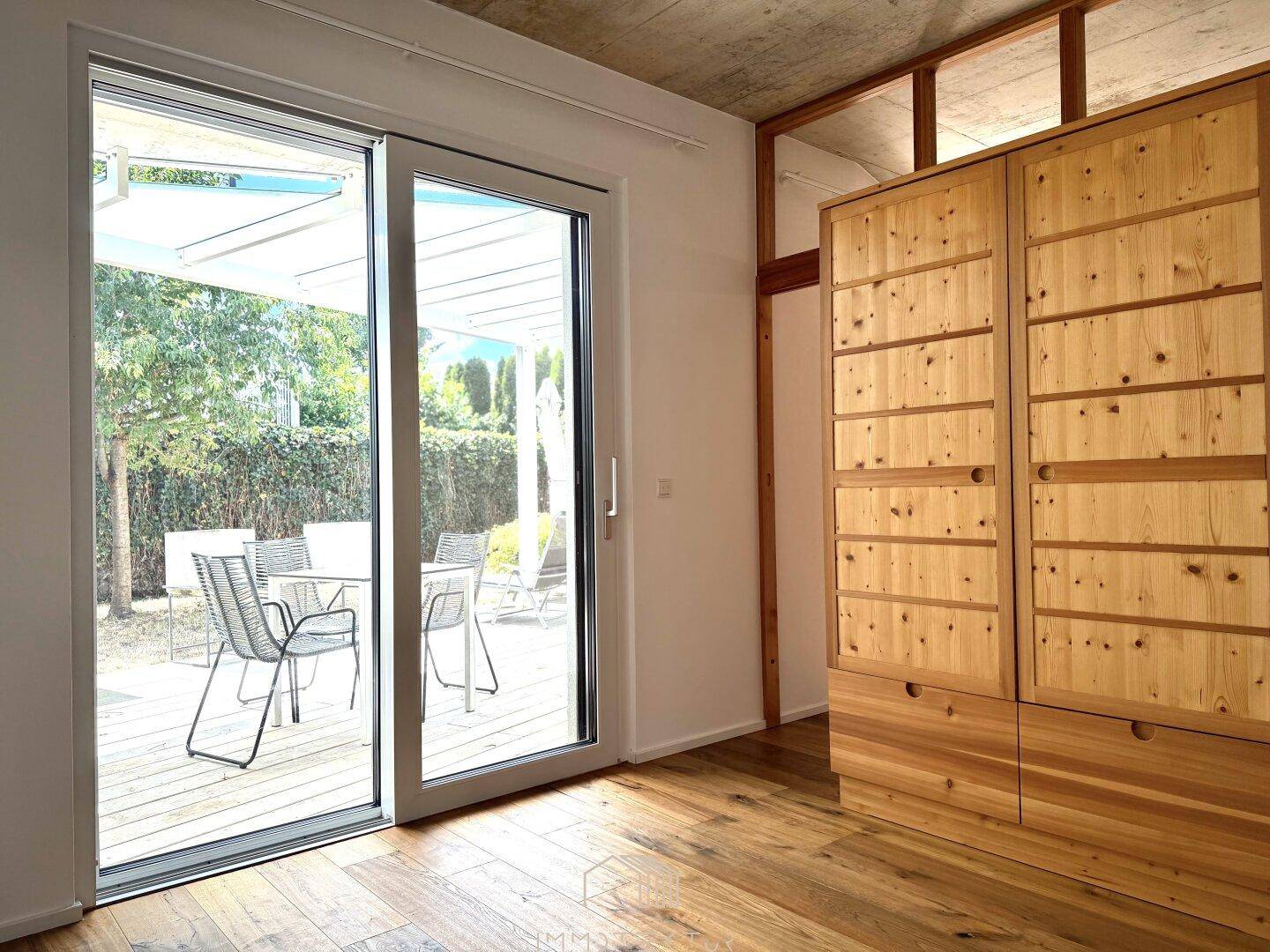 Heller Wohnraum mit Holzboden, großem Holzschrank und Schiebetür zur Terrasse.