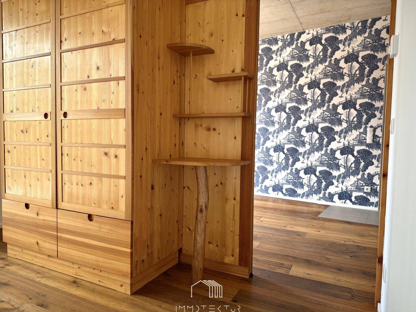 Detailansicht eines Holzschranks mit integrierten Regalen und dekorativer Tapete im Hintergrund.