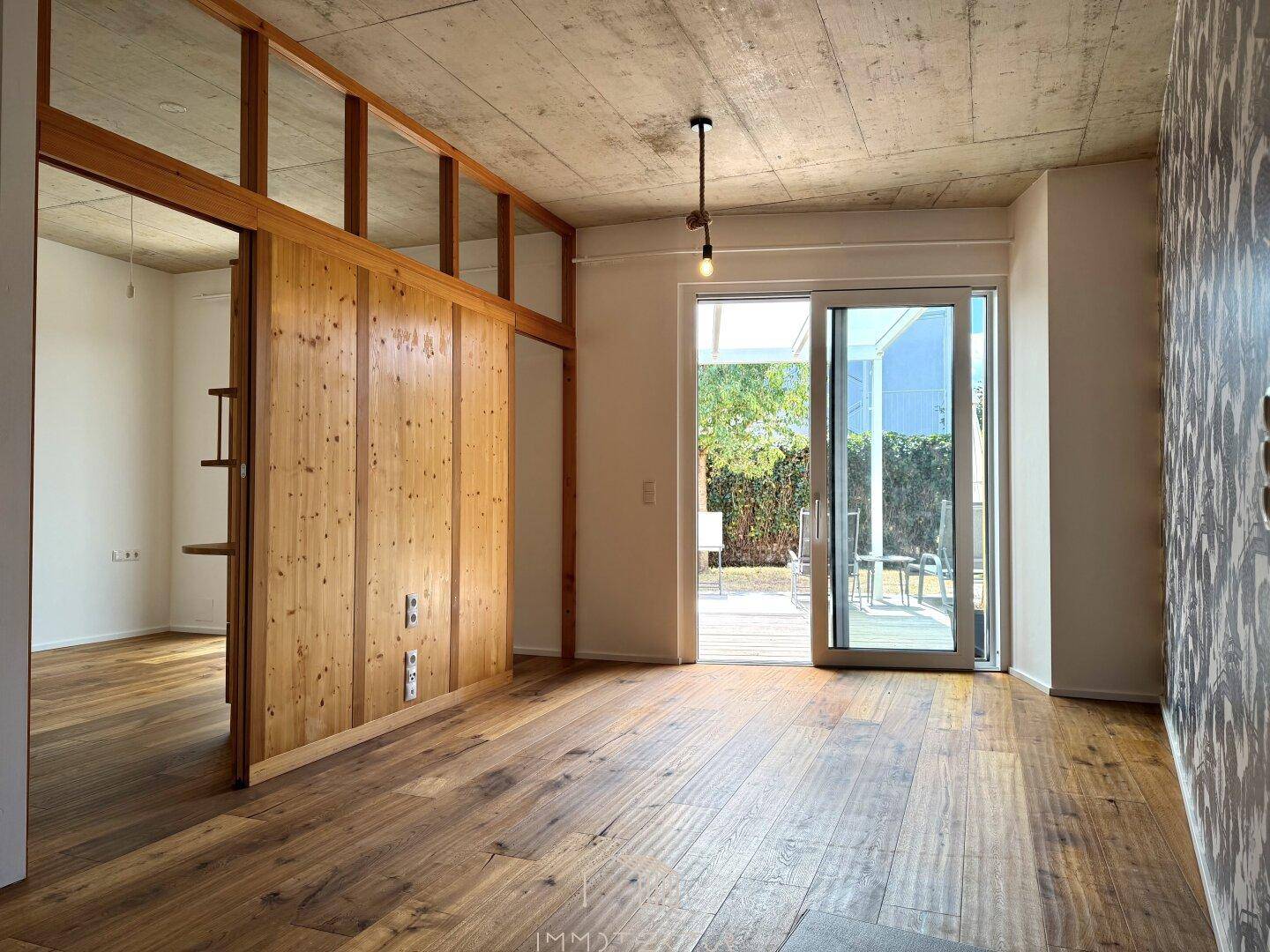 Heller Wohnraum mit Holzboden, Sichtbetondecke und Zugang zur Terrasse.