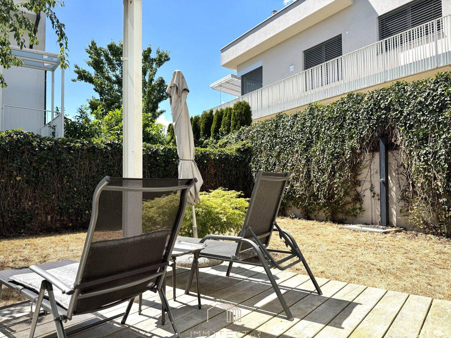 Gartenbereich mit Rasenfläche, grünen Büschen und Blick auf die moderne Gebäudefassade.